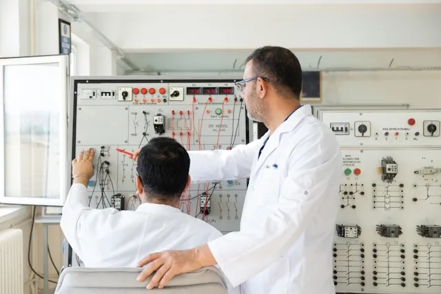two people in lab coat pointing at electrical boxes